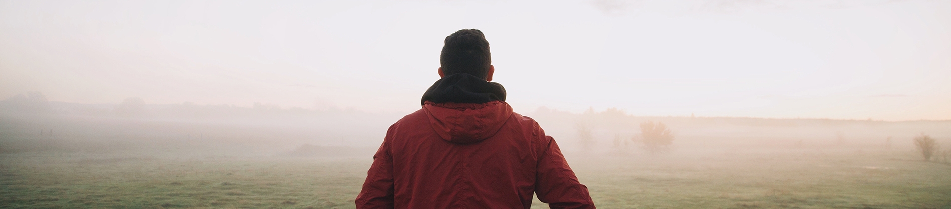 A man in a red jacket walking into a foggy field A man in a red jacket walking into a foggy field