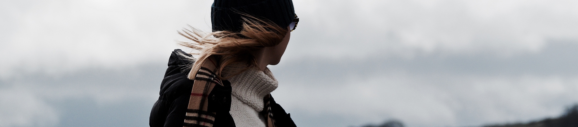 A women in a hat and scarf looking into the distant, her hair blowing in the wind A women in a hat and scarf looking into the distant, her hair blowing in the wind