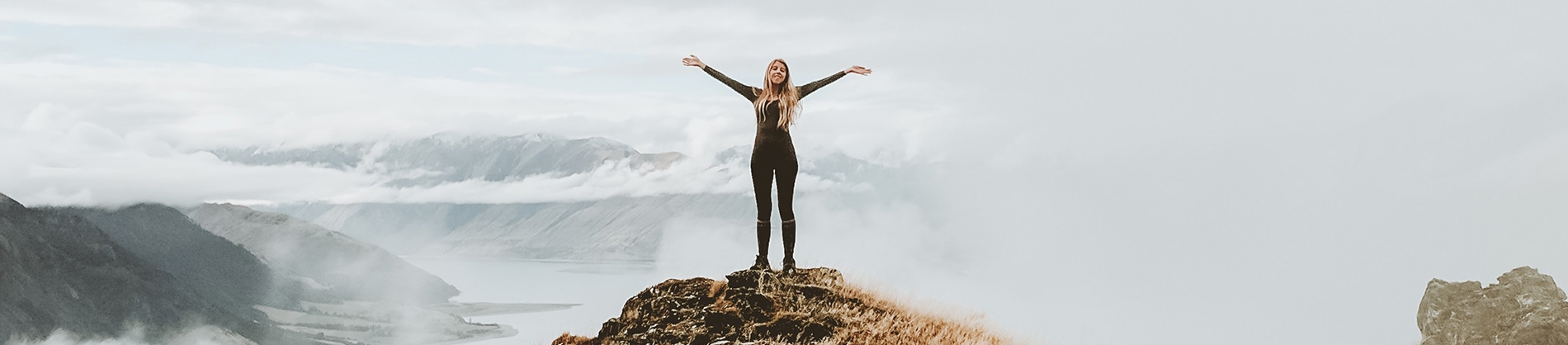 A women stood on a rock, arms open with the waves behind her