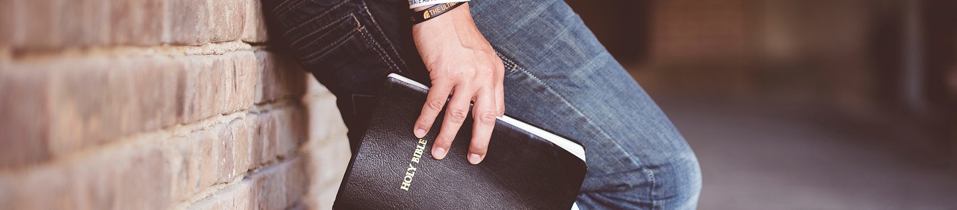 A man stood against a brick wall holding a bible A man stood against a brick wall holding a bible