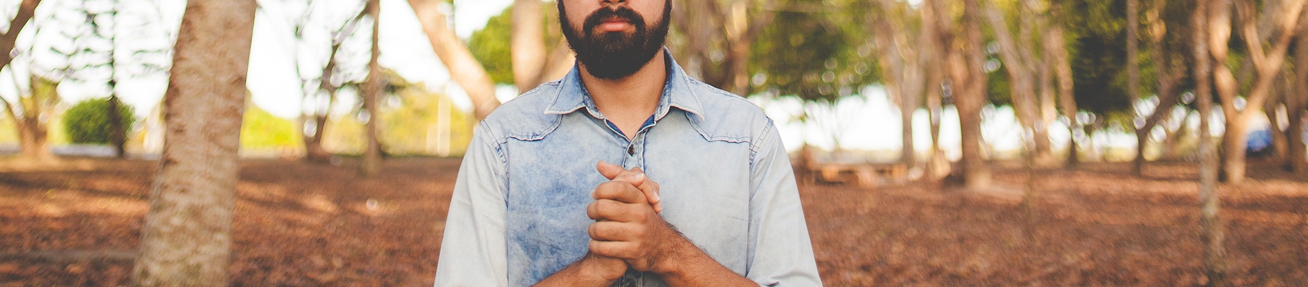 A man stood in a forest with his hand together in prayer A man stood in a forest with his hand together in prayer