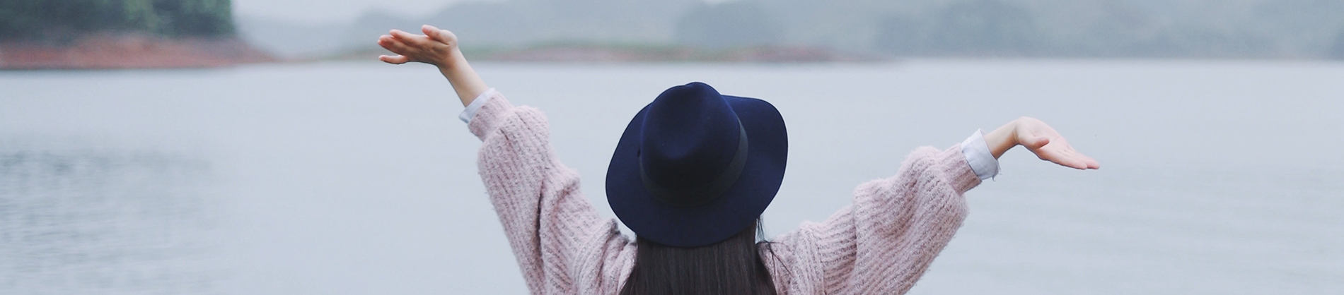 A women with her arms in the air looking over a lake A women with her arms in the air looking over a lake