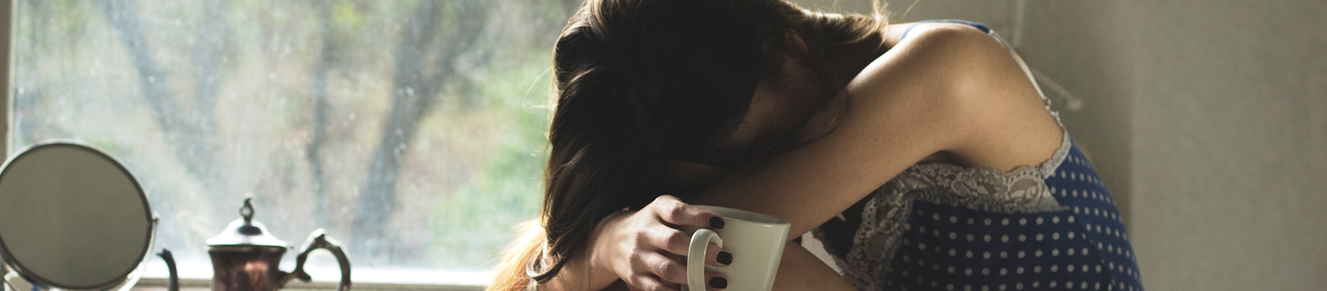 A women crying into her lap holding a mug