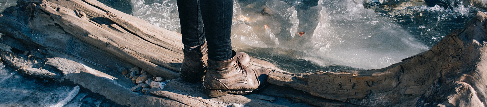 A girl in brown boots stood on a large piece of wood in the water A girl in brown boots stood on a large piece of wood in the water