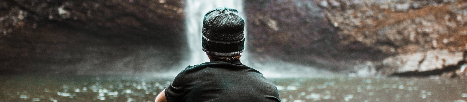 A man sat looking towards a small waterfall
