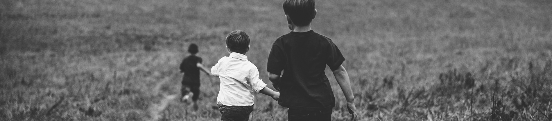 Three children running through a field together Three children running through a field together