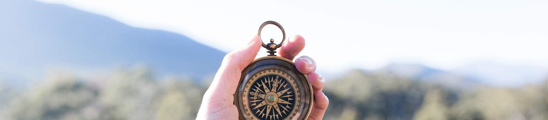 A hand holding a compass up with a landscape behind