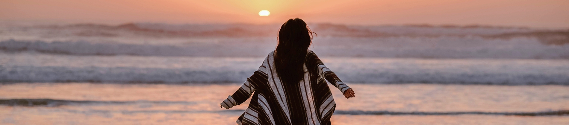 A women with her arms out beside her looking towards a sunset and the ocean