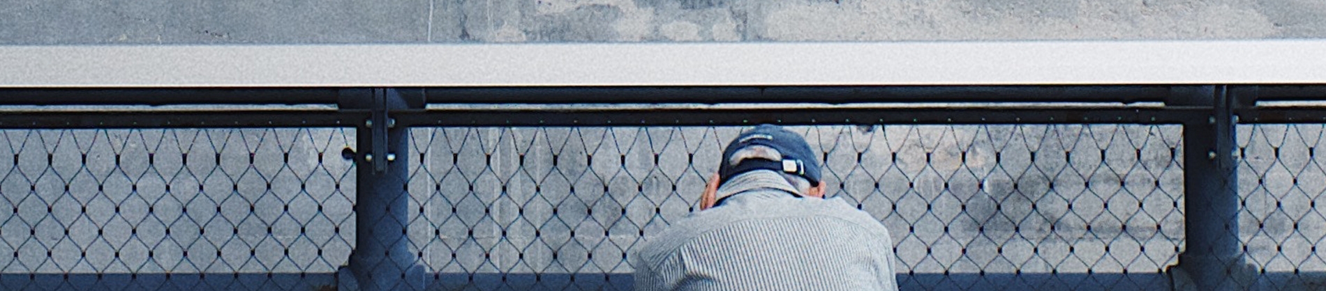 A man thinking sat on a bench opposite blue railings A man thinking sat on a bench opposite blue railings