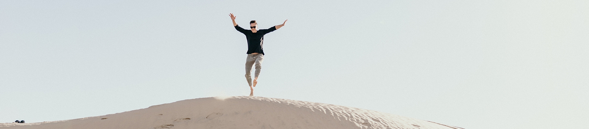 A man jumping down a sand dune with his hands in the air A man jumping down a sand dune with his hands in the air