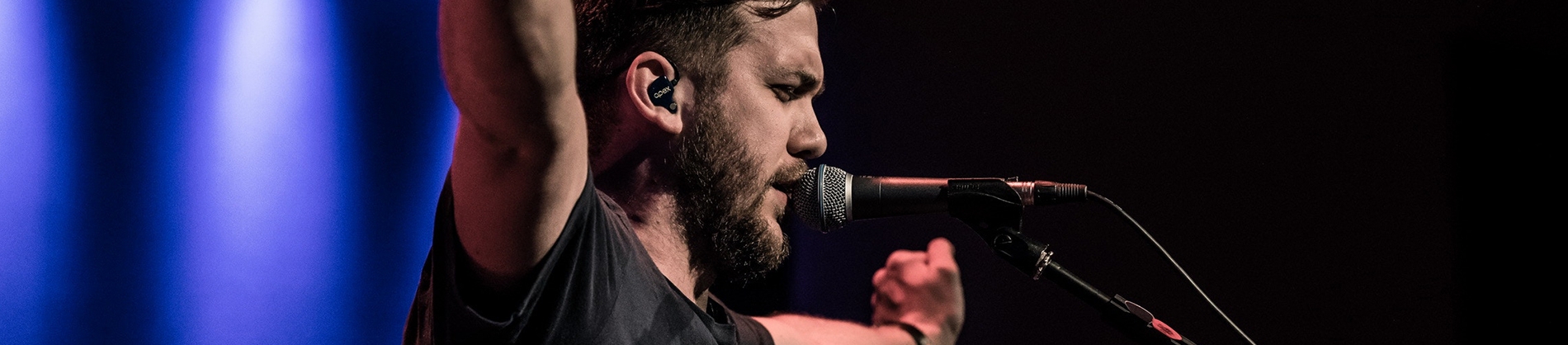 A man with his arms out speaking into a microphone on stage A man with his arms out speaking into a microphone on stage