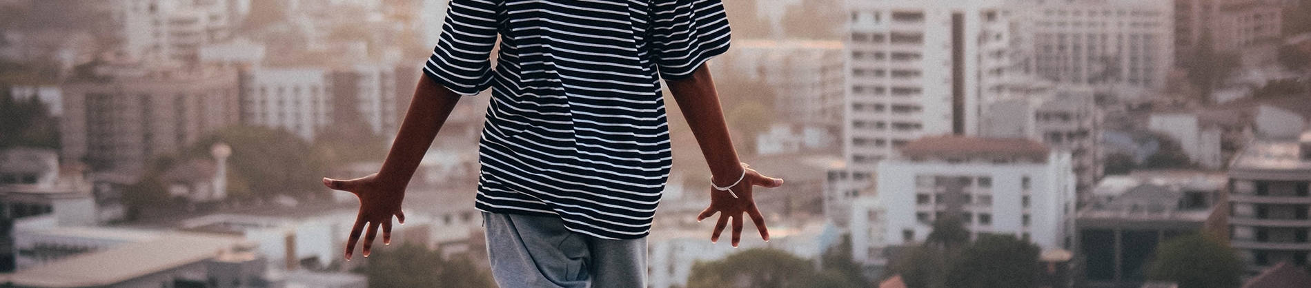 A man stood with his arms open, palms facing the sky with a city landscape in front of him A man stood with his arms open, palms facing the sky with a city landscape in front of him