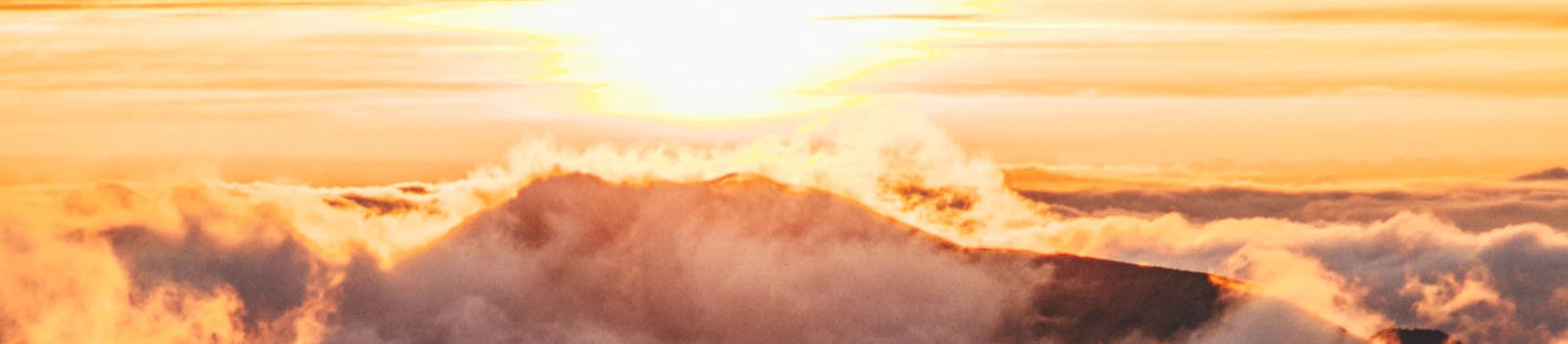 The sun rising over clouds and mountains