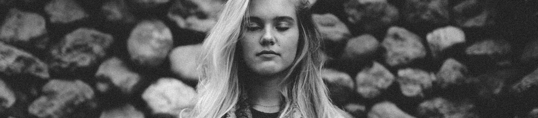 A black and white photo of a woman with her eyes closed stood in front of a brick wall A black and white photo of a woman with her eyes closed stood in front of a brick wall