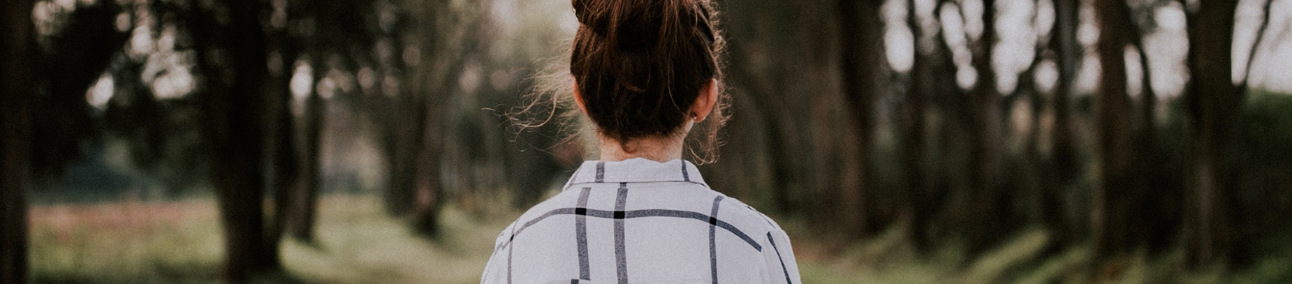A women in a checked shirt walking through a forest area A women in a checked shirt walking through a forest area