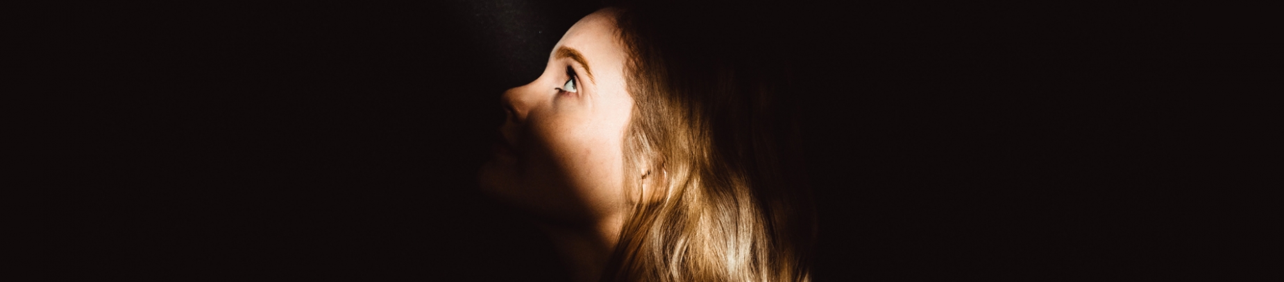 A girl in a dark room with a ray of light on her face A girl in a dark room with a ray of light on her face