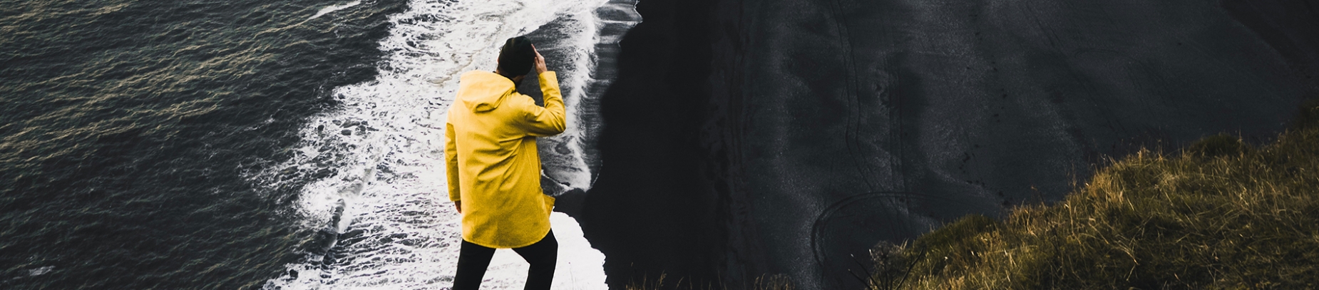 A man in a yellow coat looking over a cliff A man in a yellow coat looking over a cliff