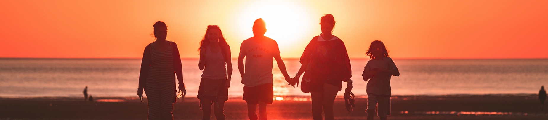 A family walking down the beach with the sunset behind them A family walking down the beach with the sunset behind them