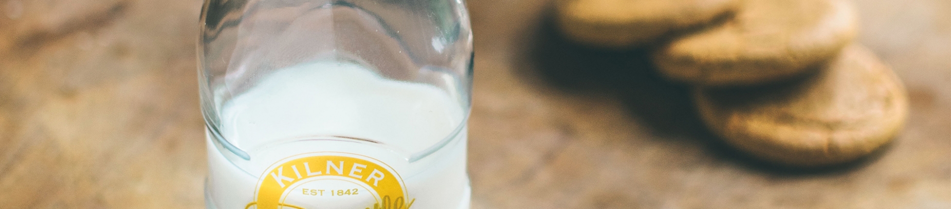 A glass bottle of milk on a table with biscuits A glass bottle of milk on a table with biscuits