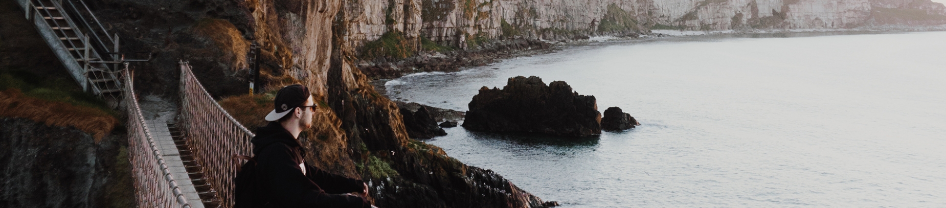 A guy stood on a rope bridge looking over the ocean A guy stood on a rope bridge looking over the ocean