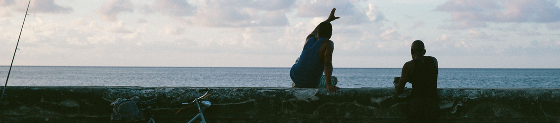 A man sat on a wall pointing to the sky, with another man stood by the wall A man sat on a wall pointing to the sky, with another man stood by the wall