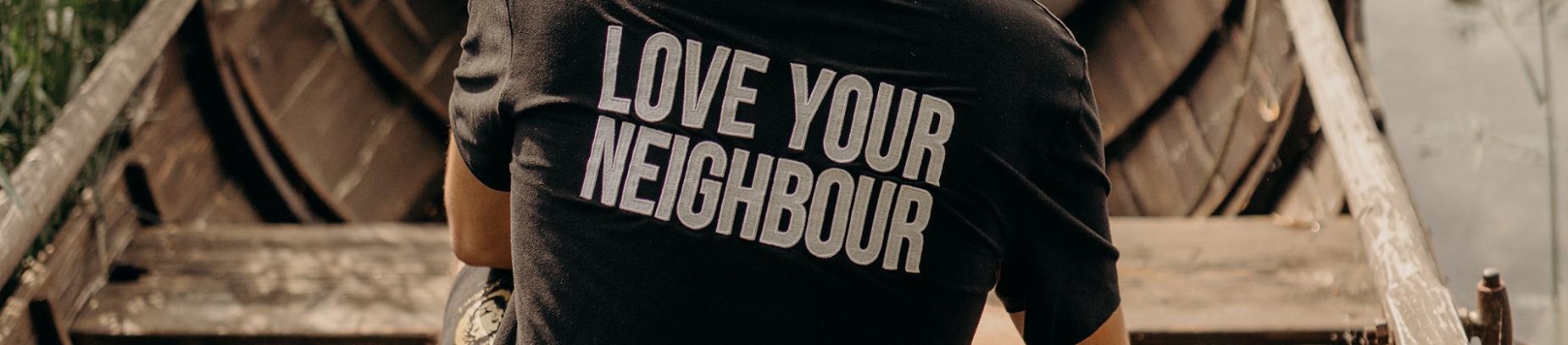 A man sat in a wooden boat wearing a 'Love Your Neighbour' top A man sat in a wooden boat wearing a 'Love Your Neighbour' top