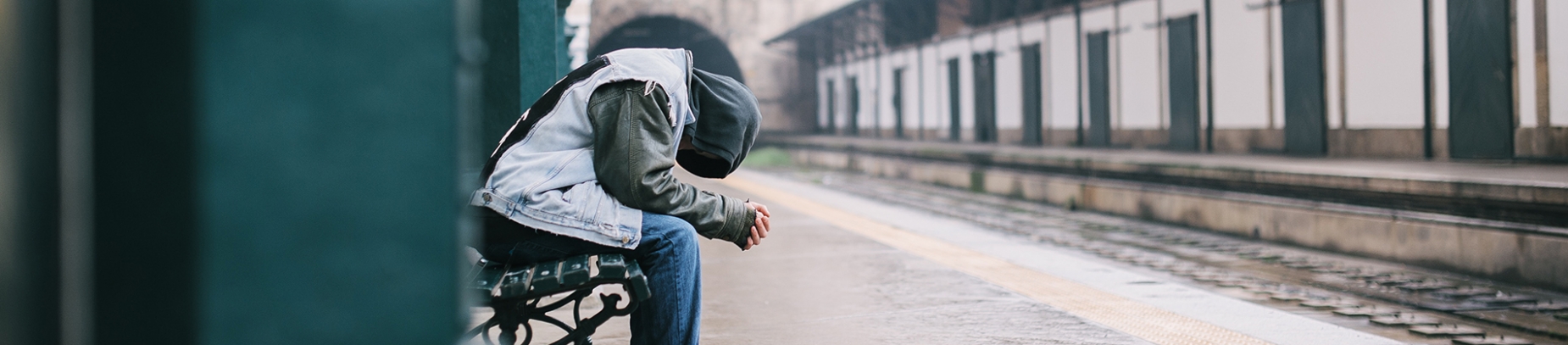 A man sat ay a train stop bowing his head into his hands A man sat ay a train stop bowing his head into his hands