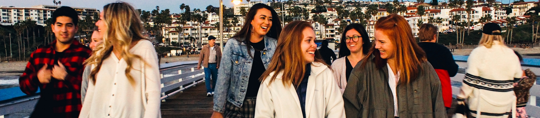 A group of friends smiling and talking while walking down a pier A group of friends smiling and talking while walking down a pier