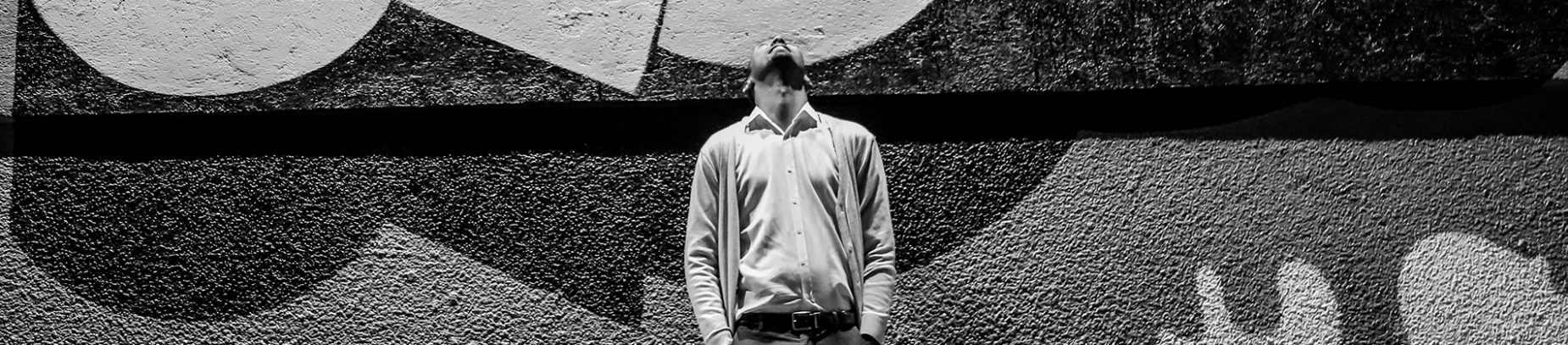 A black and white photo of a man looking up to the sky with a painted wall behind him A black and white photo of a man looking up to the sky with a painted wall behind him