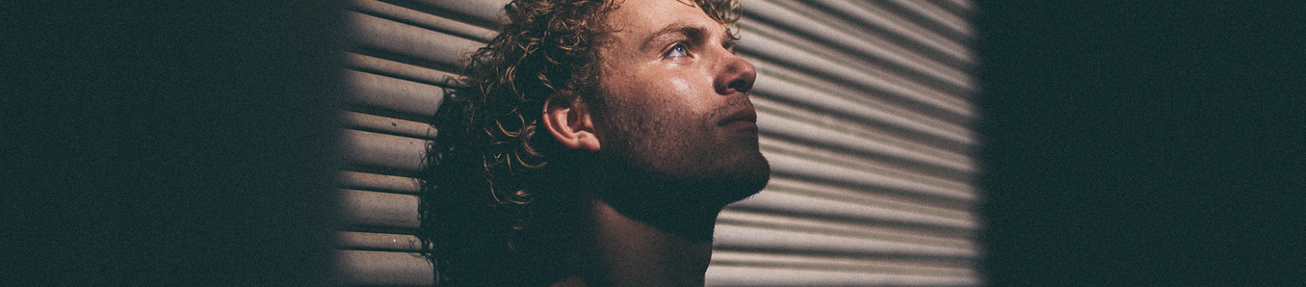 A man stood against a wall with the light from a window shining on him A man stood against a wall with the light from a window shining on him