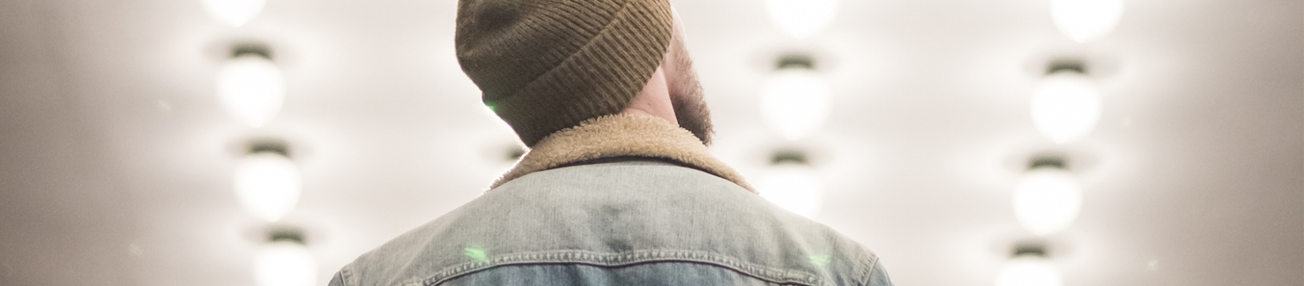 A man in a jacket and hat looking up at bright lights A man in a jacket and hat looking up at bright lights