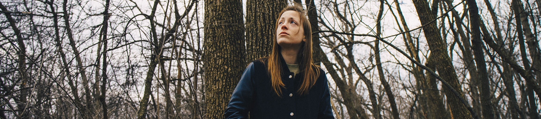 A women sat in a forest looking up to the grey sky A women sat in a forest looking up to the grey sky