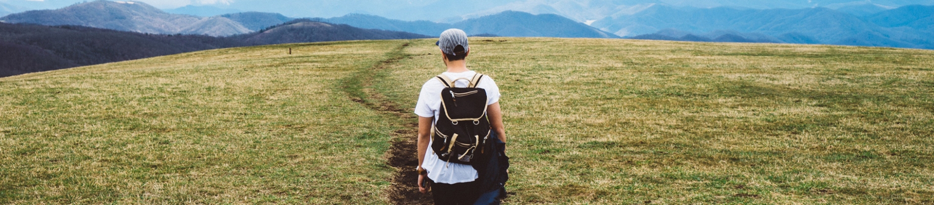 A guy walking down a grass path wearing a backpack A guy walking down a grass path wearing a backpack