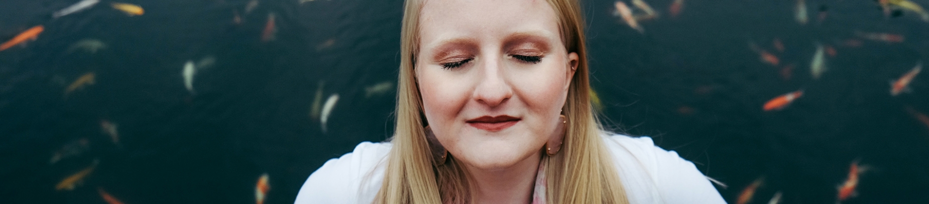 A woman with her eyes closed, stood in front of a pond A woman with her eyes closed, stood in front of a pond
