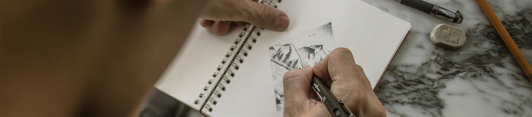 A man drawing in a sketchbook on a marble table