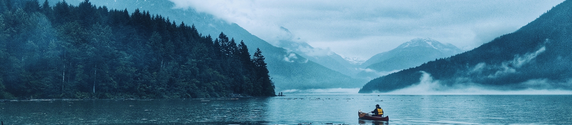 A man in a canoe rowing across a lake A man in a canoe rowing across a lake