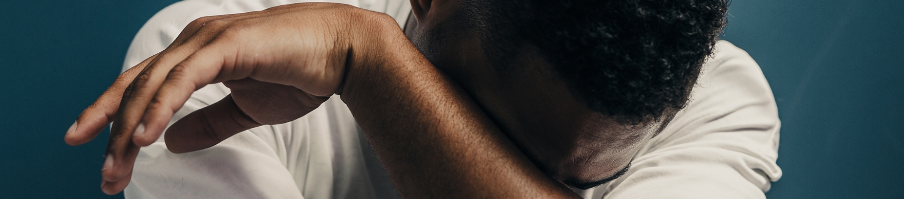 a guy in a white t-shirt hunched over crying into his arm
