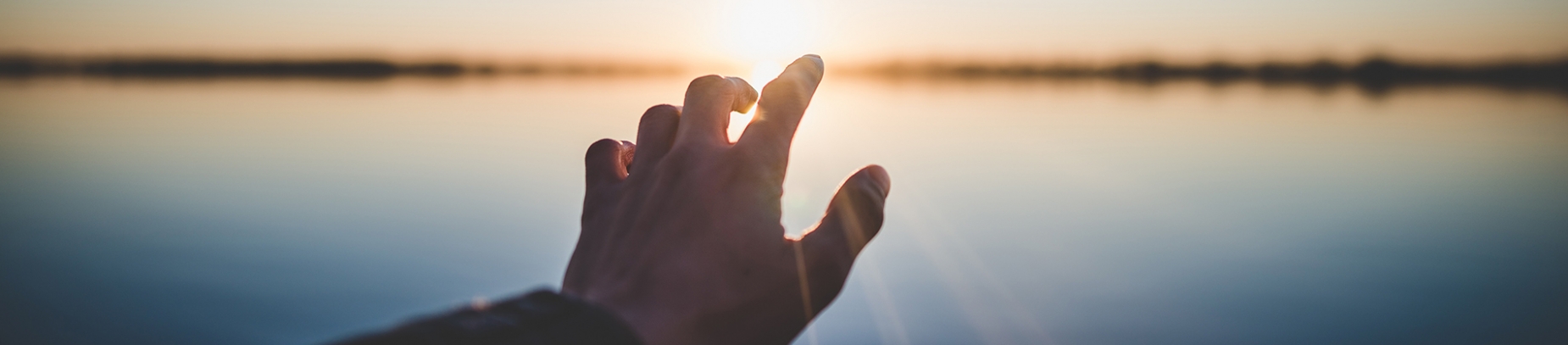 Someone reaching out their hand towards the setting sun Someone reaching out their hand towards the setting sun