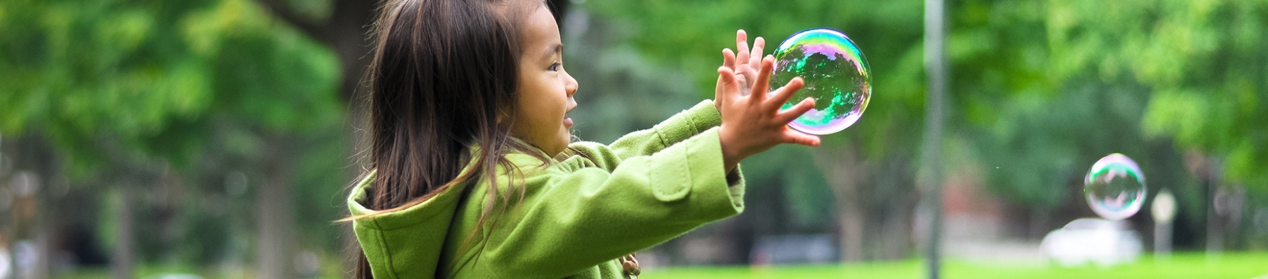 A little girl in a green coat reaching for a bubble A little girl in a green coat reaching for a bubble