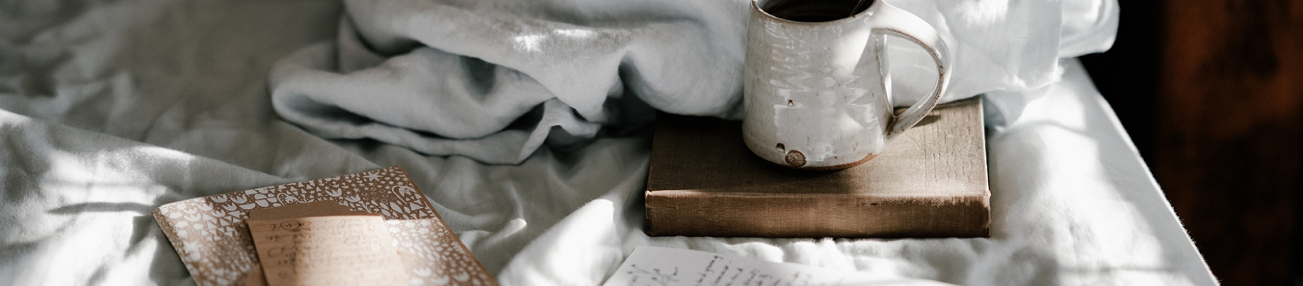 A large book, notebooks and mug resting on bed sheets A large book, notebooks and mug resting on bed sheets