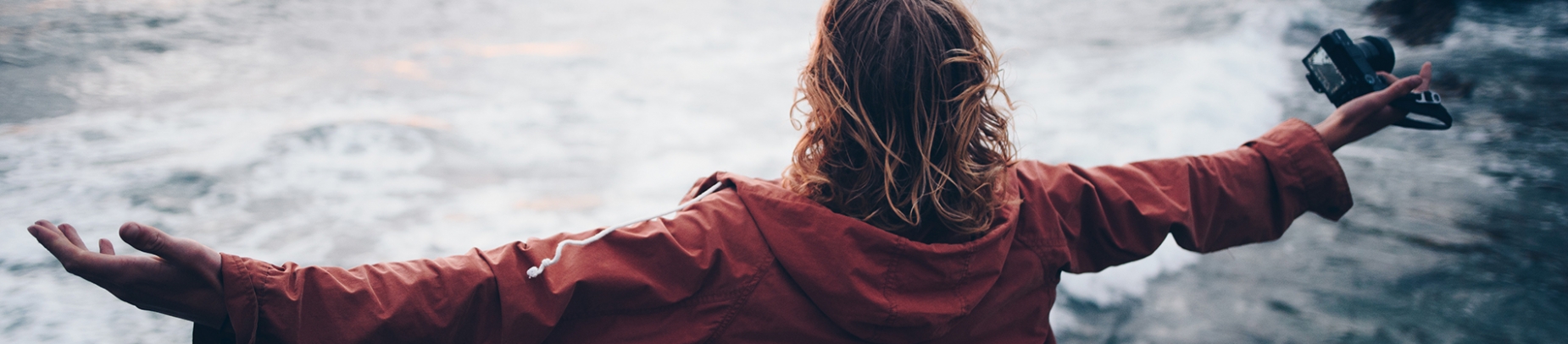 A women in a red raincoat with her arms spread wide, looking out to sea A women in a red raincoat with her arms spread wide, looking out to sea