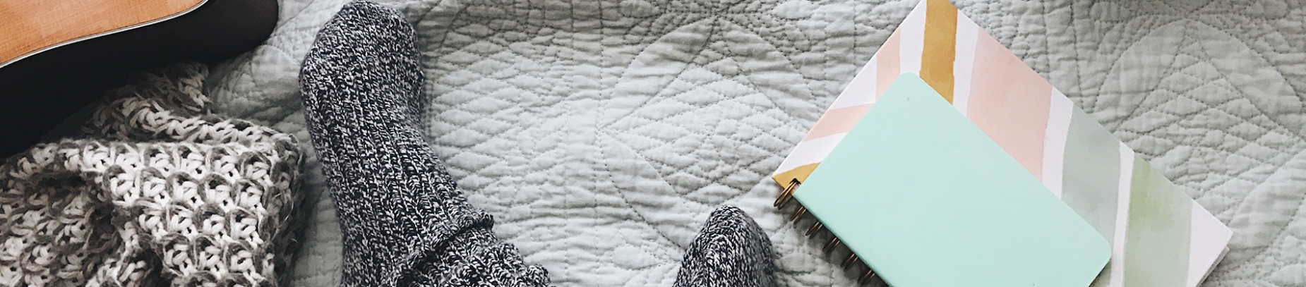 Women's feet in socks, notebooks and a guitar on a bed