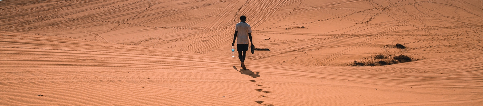 A man walking through the desert holding shoes and water A man walking through the desert holding shoes and water