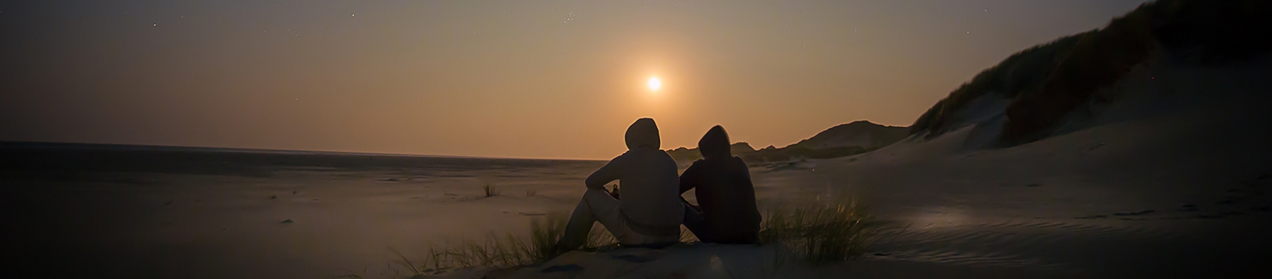 Two people sat on a beach watching the sunset Two people sat on a beach watching the sunset
