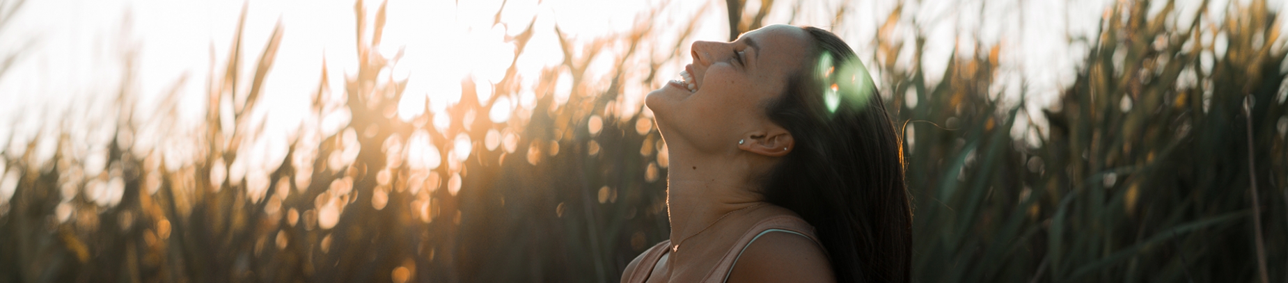 A women stood in long grass smiling at the sky A women stood in long grass smiling at the sky