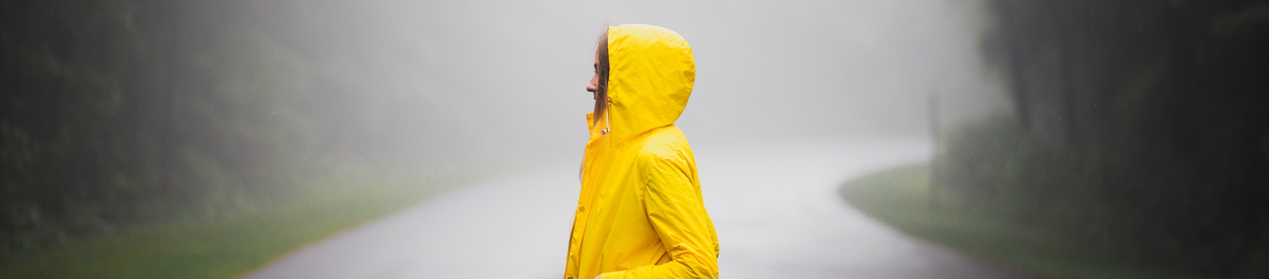 A girl in a bright yellow coat stood on a road in the rain and mist A girl in a bright yellow coat stood on a road in the rain and mist
