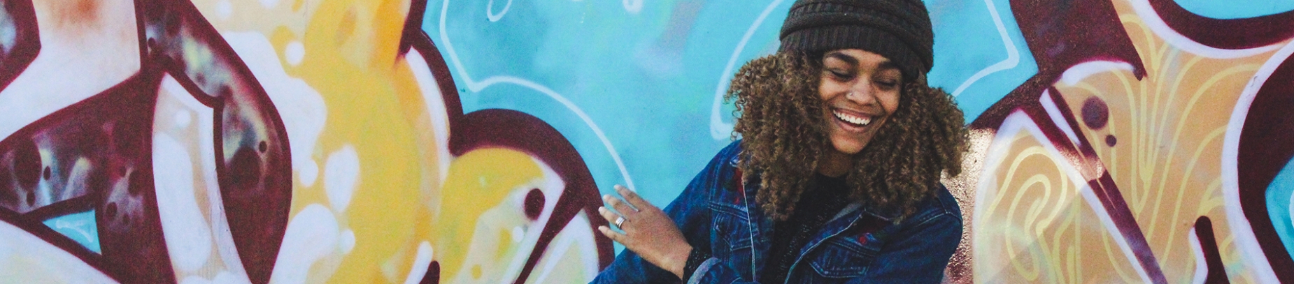 A women stood in front of a graffiti wall smiling A women stood in front of a graffiti wall smiling