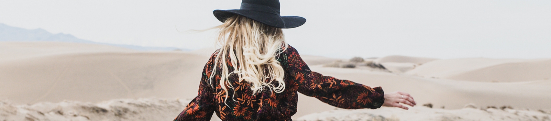 A women in a black and orange dress walking over sand dunes A women in a black and orange dress walking over sand dunes