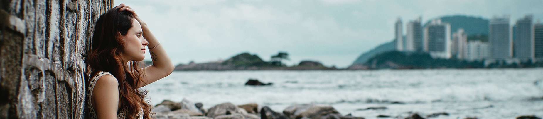 A women leaning against a wall by the sea with her hand on her head A women leaning against a wall by the sea with her hand on her head
