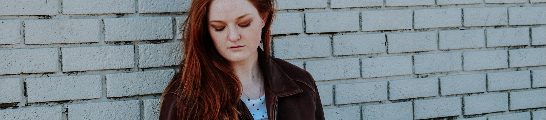A women leaning against a brick wall looking down at the ground A women leaning against a brick wall looking down at the ground
